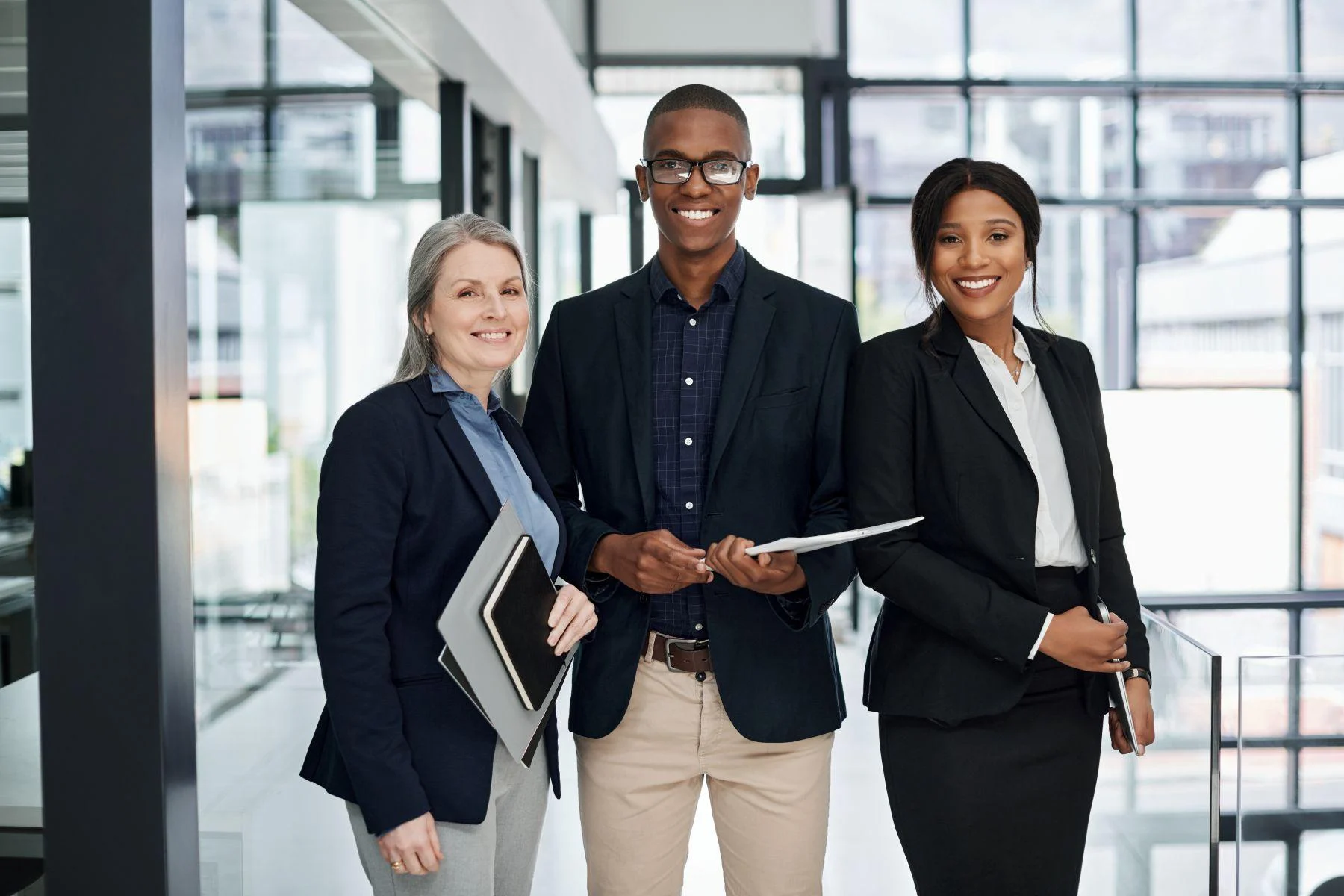 Three-business-professionals-smiling-in-an-office-corridor-holding-tablets.webp