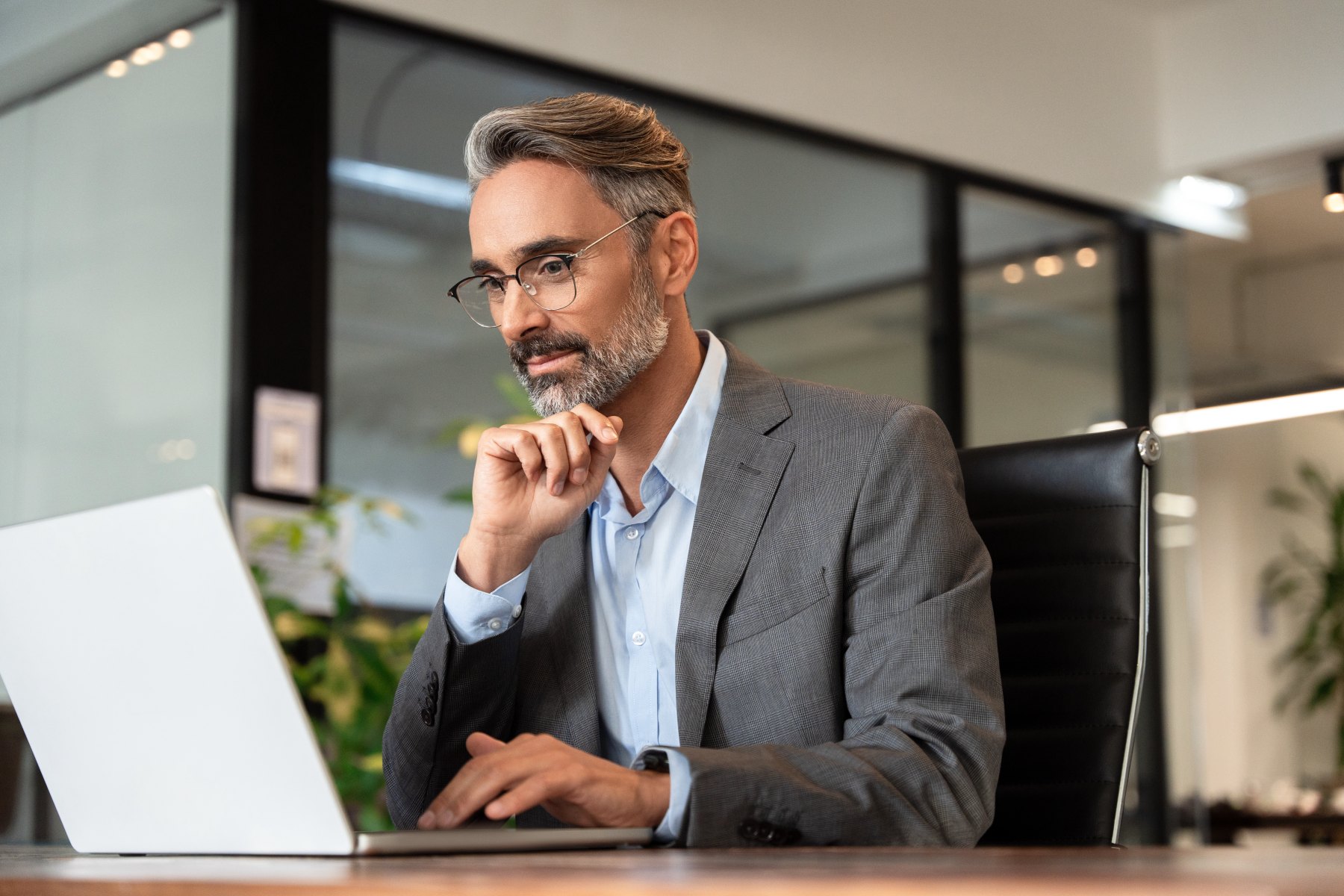 mature-businessman-in-suit-thinking-at-laptop-in-modern-office.jpeg